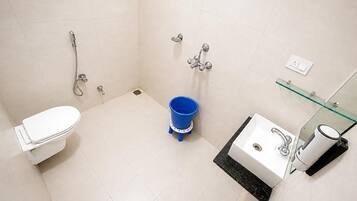 Un baño con inodoro, lavamanos, cabina de ducha de vidrio y un cubo azul.