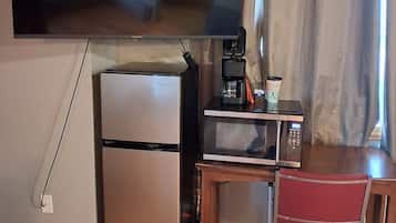 A compact kitchenette with a refrigerator, microwave, and coffee maker on a wooden table.