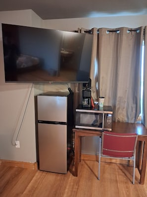 A compact kitchenette with a refrigerator, microwave, and coffee maker on a wooden table. - Cyclone Lodge By Fresh Stay (Harlan)