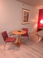 Una habitación con una mesa redonda de madera, dos sillas tapizadas de rojo, un cuadro en la pared, una pared roja y una lámpara sobre una mesita de noche.