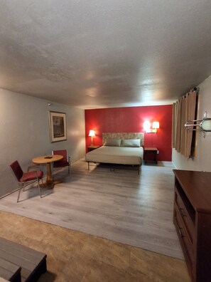 A bedroom with a bed, a bedside table, a lamp, a chair, a small table, and a dresser.