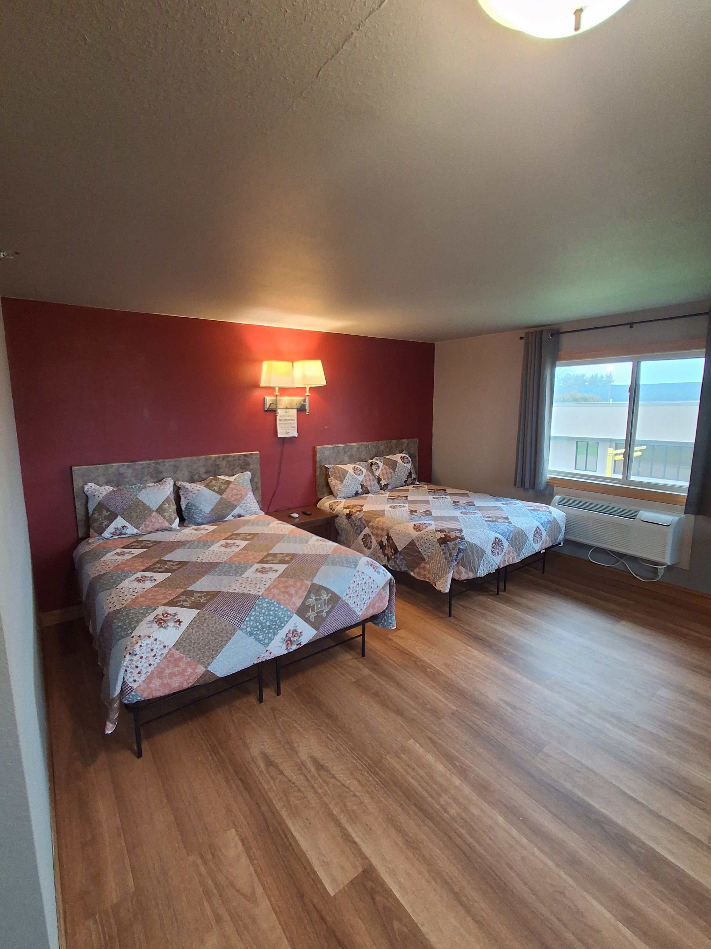 Une chambre avec deux lits, un mur rouge, une fenêtre donnant sur un paysage agréable et un luminaire au plafond.