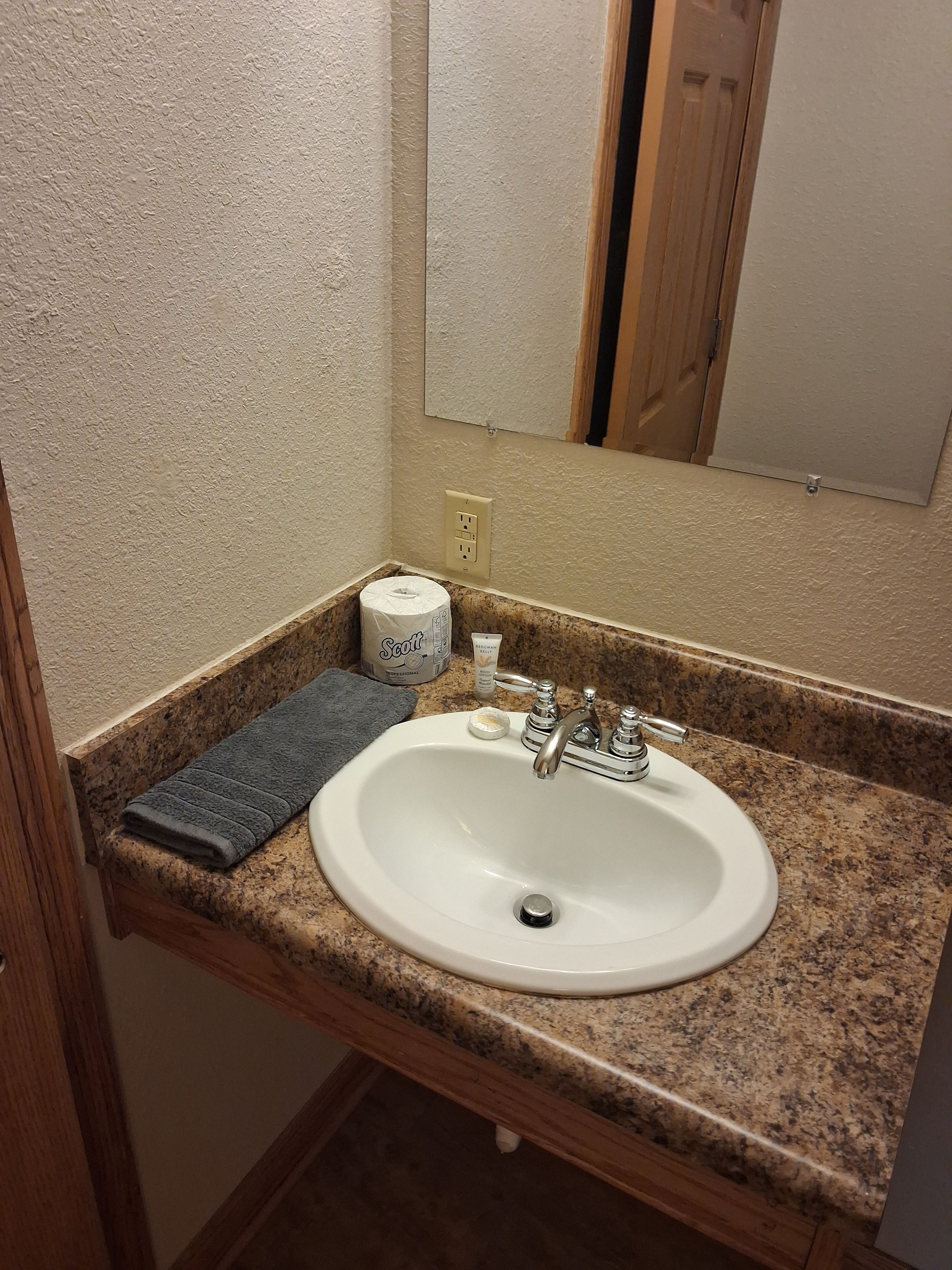 A bathroom with a white sink, granite countertop, a towel, toilet paper, and a mirror.