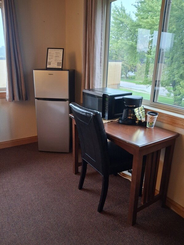 Habitación de hotel compacta con kitchenette, una mesa de comedor, una silla y ventana con vistas a árboles y una carretera.