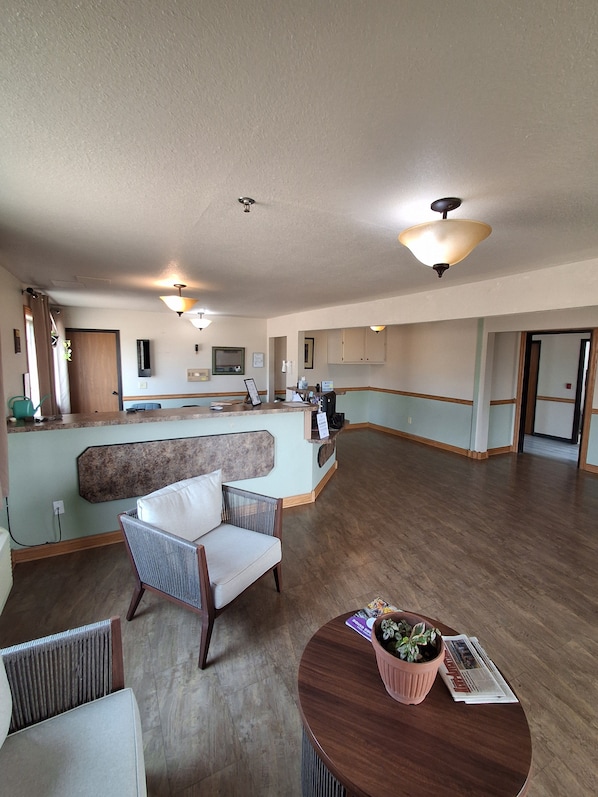 A spacious living area with a kitchen in the background, a reception desk, and a seating area with a round table and chairs. - Cyclone Lodge By Fresh Stay (Harlan)