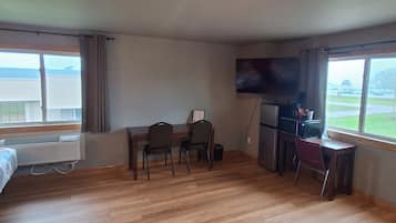 A hotel room with a wooden floor, a bed, a desk with chairs, a television, and a window with a view.
