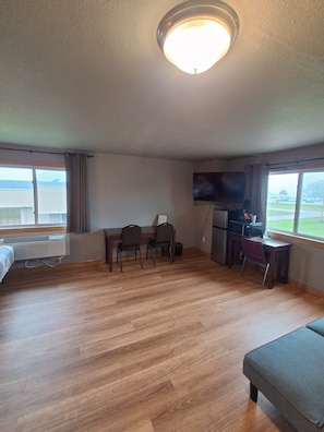 A hotel room with a wooden floor, a bed, a desk with chairs, a television, and a window with a view.