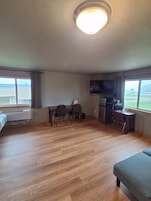 Habitación de hotel con piso de madera, una cama, un escritorio con sillas, televisor y ventana con vista.