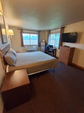 Habitación de hotel con cama, escritorio, cómoda, televisor y ventana con vistas.