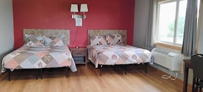 A room with two beds, a nightstand, a wall-mounted light fixture, and a window with curtains.