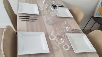 Een eettafel gedekt met witte borden, bestek en wijnglazen, met daarboven een lijst met een foto.