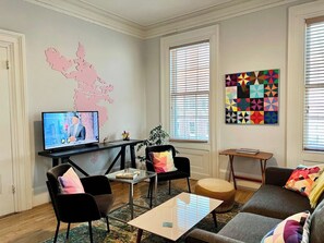 Ein Wohnzimmer mit Fernseher, einer Karte an der Wand, einem farbenfrohen geometrischen Kunstwerk und einem Sofa.