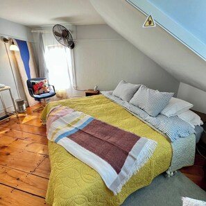Ein Schlafzimmer mit einem Bett, einem Sessel, einem Ventilator und einem Fenster.