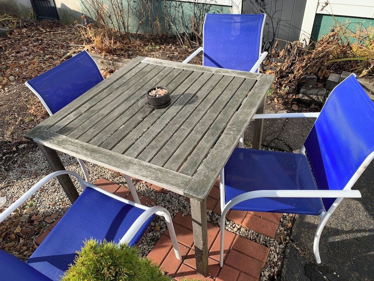 Ein quadratischer Holztisch mit einer Schüssel, umgeben von vier blauen Stühlen.