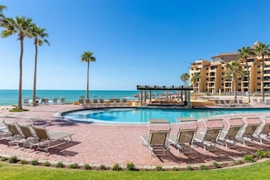 A resort pool area with lounge chairs, a cabana, and a view of the ocean. - Cozy Ground Level Condo w/ Pool | Princesa E-103 (Puerto Peñasco)