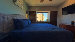 Quarto com cama, cômoda, televisão e janela com vista para edifícios.