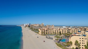 Un hôtel situé sur la côte, composé de plusieurs bâtiments, avec une plage et un ciel d’un bleu limpide.