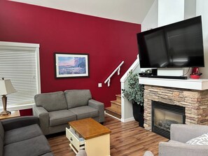 A living room with a grey sofa, a television on a white stand, a fireplace, and a red accent wall.