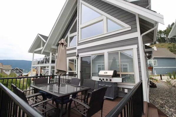 A modern house with a deck, a grill, and a glass table.