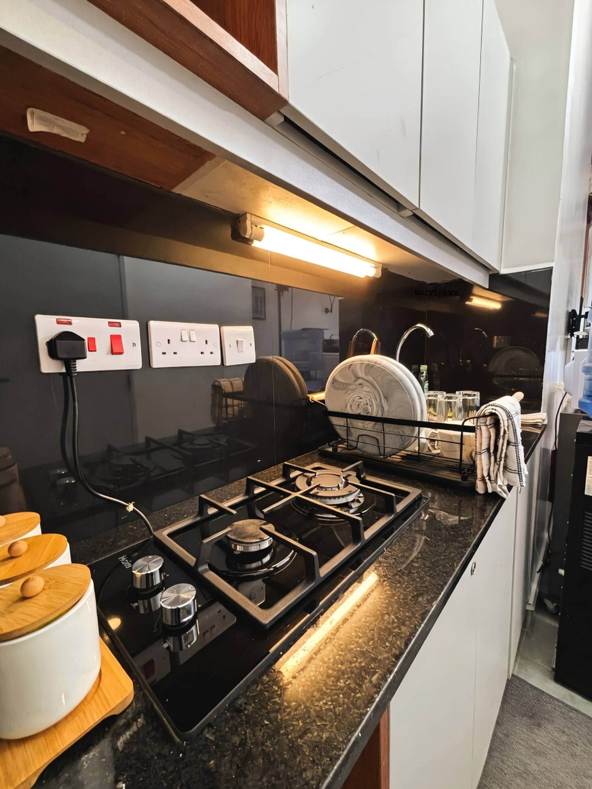 Una cocina moderna con estufa a gas, tabla de cortar de madera y hervidor blanco.