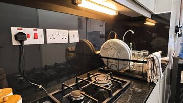 Una cocina moderna con estufa a gas, tabla de cortar de madera y hervidor blanco.