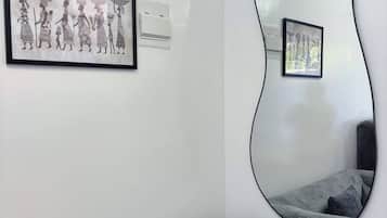 Uma sala de estar moderna com um sofá cinzento, um espelho grande e duas obras de arte emolduradas na parede.