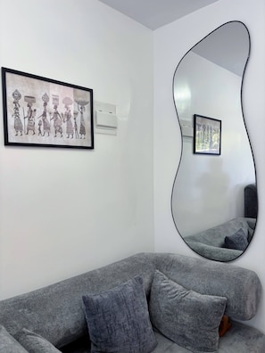 Una sala moderna con un sofá gris, un espejo grande y dos cuadros enmarcados en la pared.