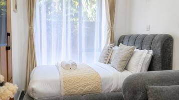 Quarto moderno com cama, sofá revestido de cinza e mesa de cabeceira de madeira com controle remoto.