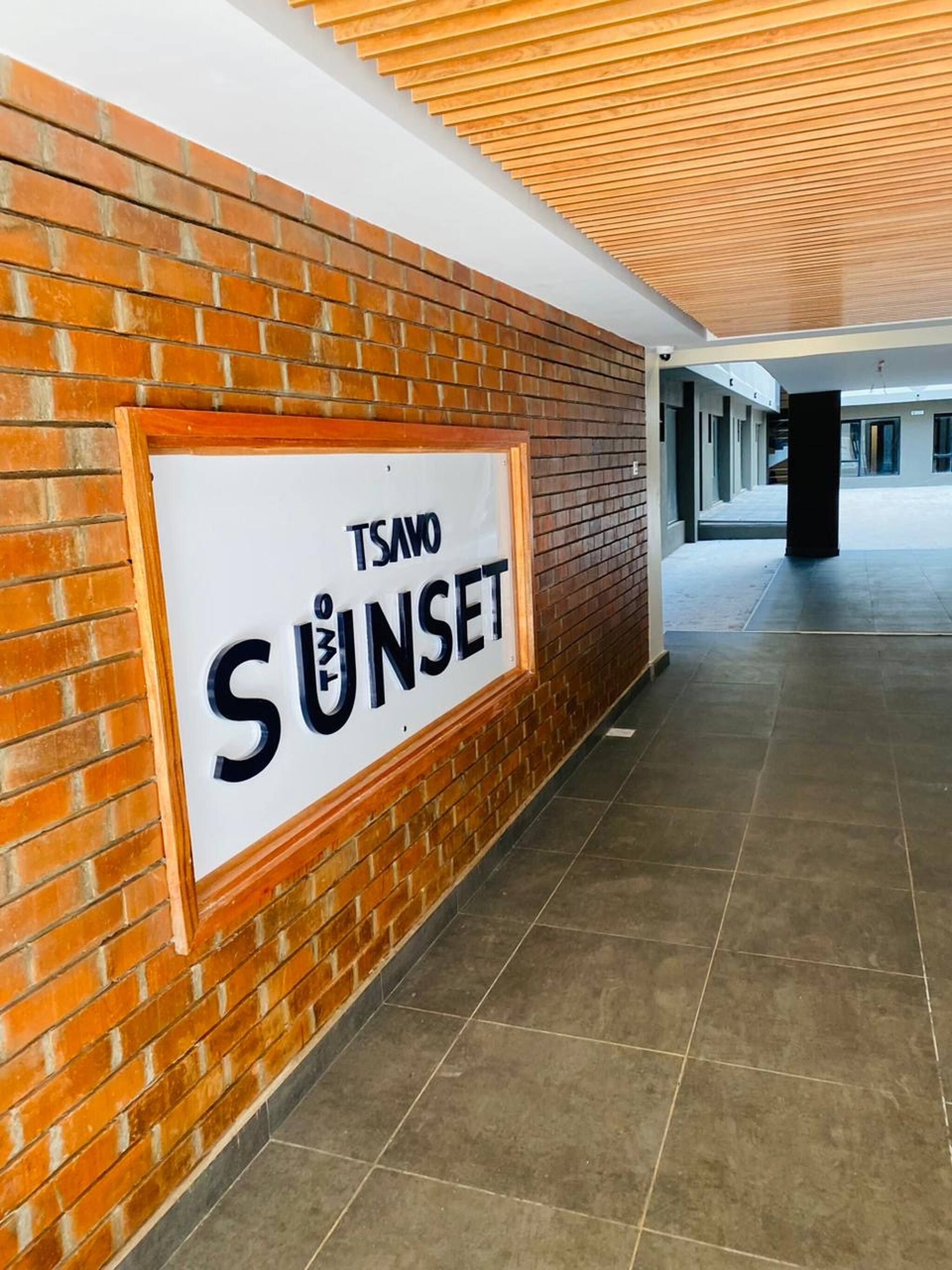 A corridor with a sign reading 'TSAVO SUNSET' on a brick wall.