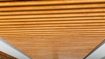 A corridor with a wooden slatted ceiling, brick walls, and a glass door at the end.