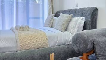 Un dormitorio moderno con una cama, un sofá gris y una mesa de centro de madera con una botella.