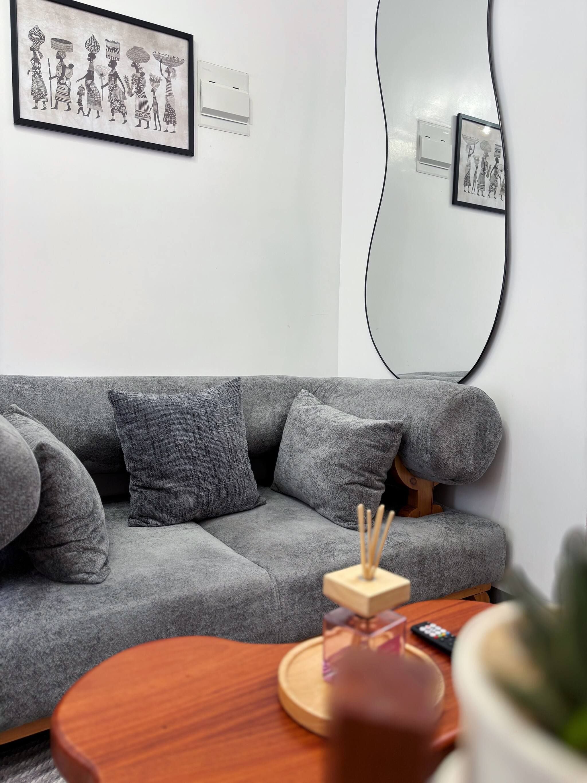Una sala de estar moderna con un sofá gris, una mesa de centro redonda de madera y un espejo grande.