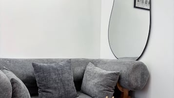 Una sala de estar moderna con un sofá gris, una mesa de centro redonda de madera y un espejo grande.
