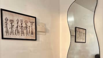 Una sala de estar moderna con un sofá gris, un espejo abstracto grande y dos obras de arte enmarcadas en la pared.