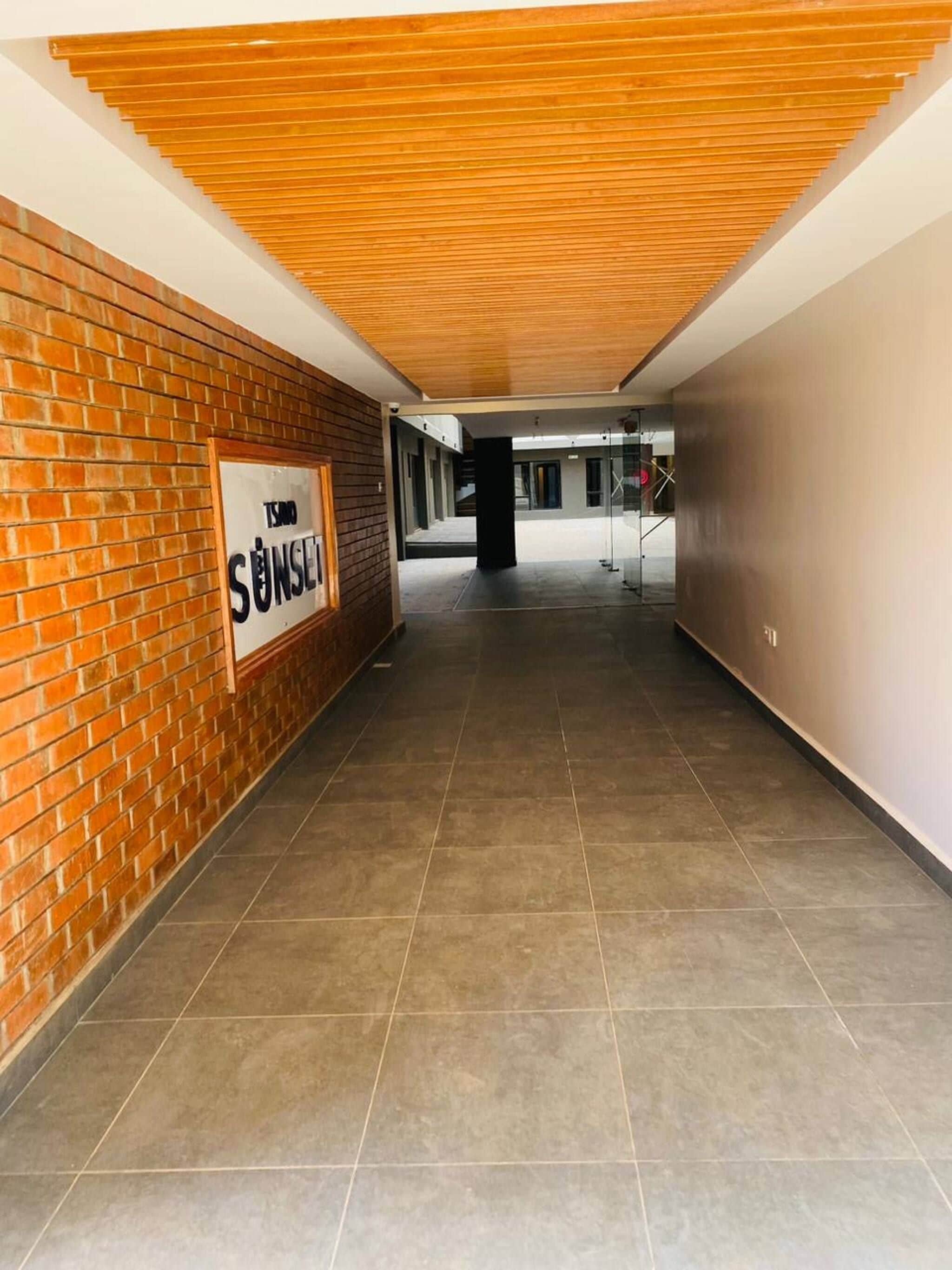 Un pasillo con una pared de ladrillo en un lado y una pared lisa en el otro, que conduce a una puerta de vidrio al final.