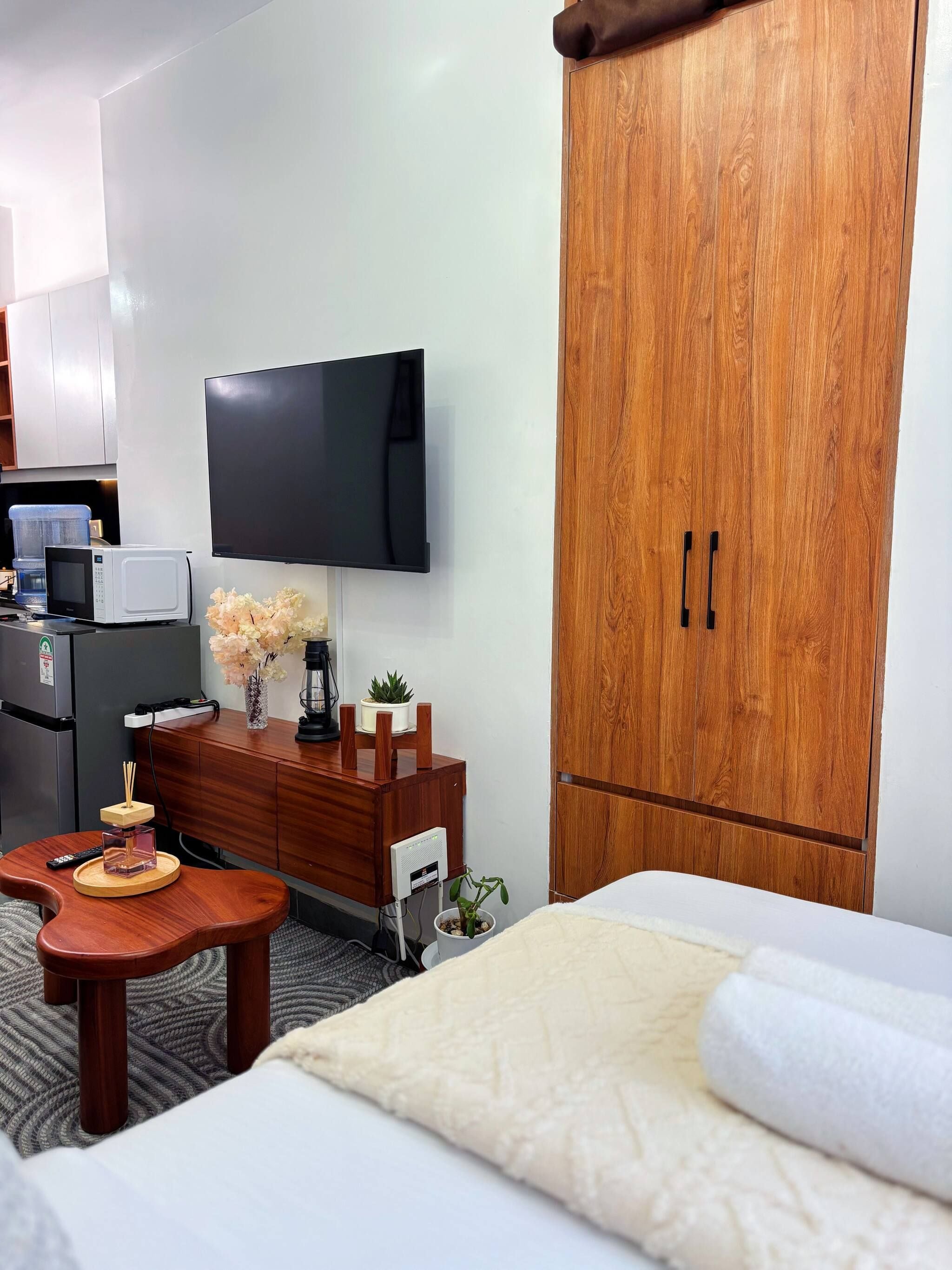 A hotel room with a bed, a wooden wardrobe, a television, a small table with a remote control, a microwave, and a potted plant.