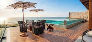 Eine Holzterrasse mit Sitzgelegenheiten im Freien, einem Pool und Blick aufs Meer.