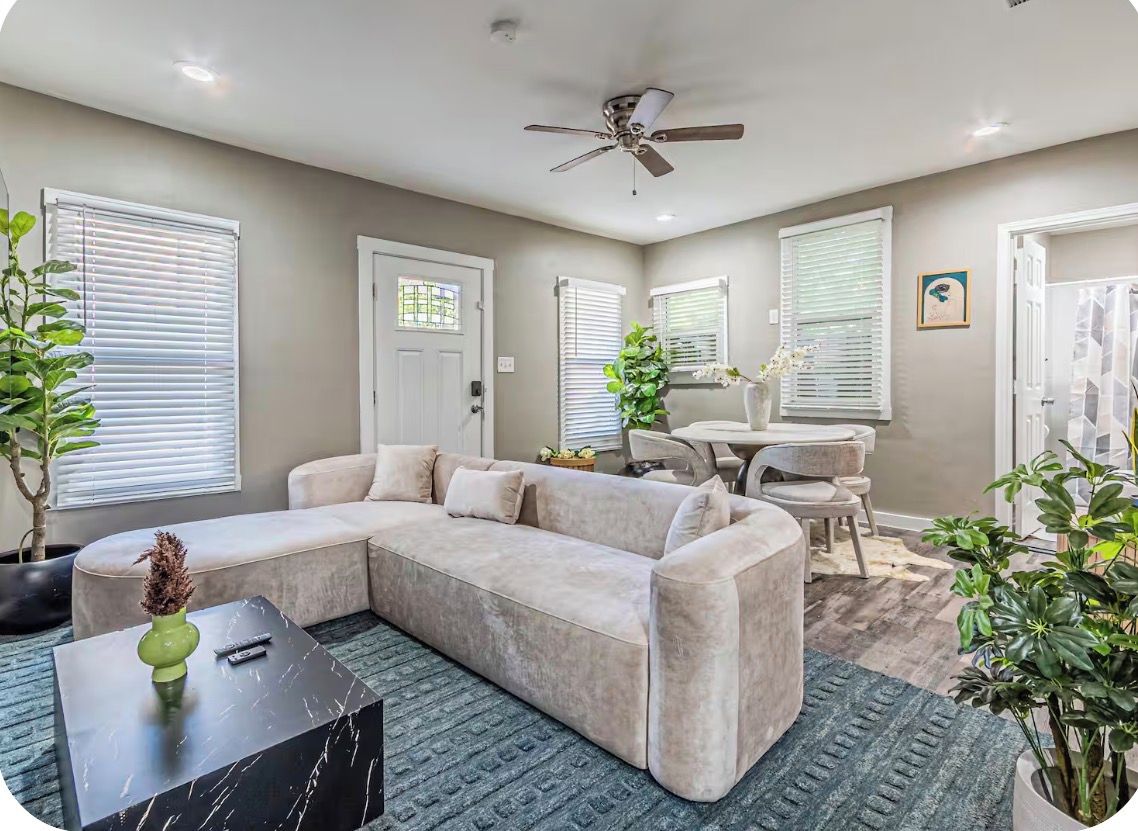 A living room with a sectional sofa, a coffee table, a ceiling fan, and a dining area with a table and chairs.