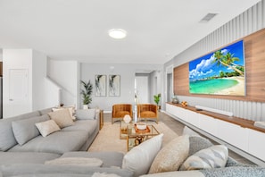 A modern living room with a large flat-screen TV, a grey sofa, two armchairs, and a coffee table. - Grand 15BR Kissimmee Estate 30 Guests (Kissimmee)