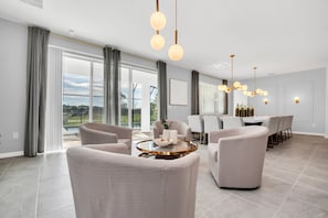 Ein geräumiges Wohnzimmer mit einem runden Couchtisch, beigen Sofas und einem Essbereich mit weißem Tisch und Stühlen.