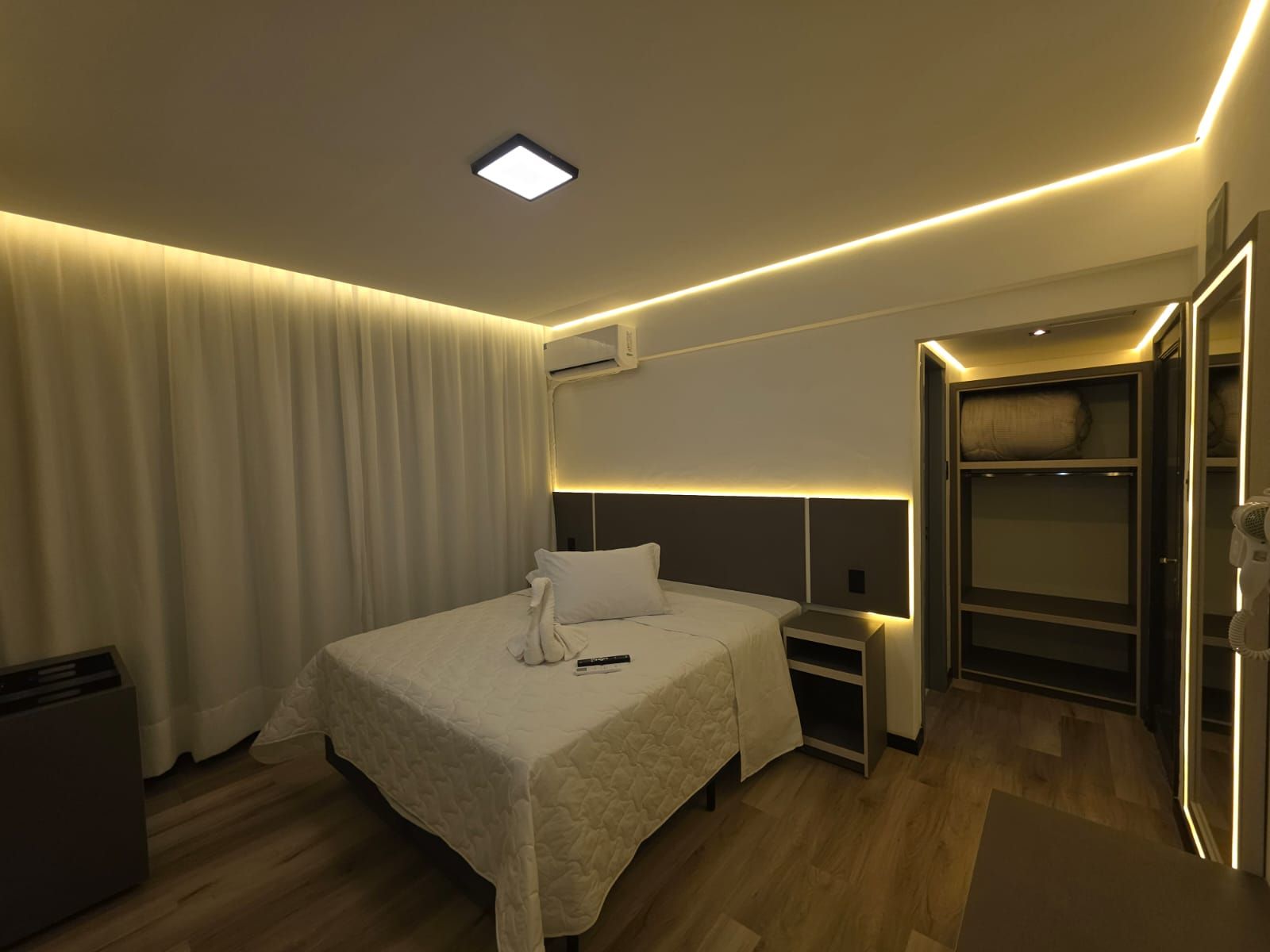 A hotel room with a bed, bedside tables, an air conditioning unit, a wardrobe, and a mirror.