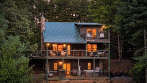 Eine zweistöckige Holzhütte mit Balkon und mehreren Fenstern, umgeben von dichtem Wald.