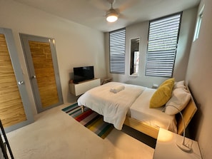 A hotel room with a bed, a television, a window with blinds, a ceiling fan, and a door. - Modern 4 bedroom loft, open-air living, private pool and power generator (Cabo Rojo)