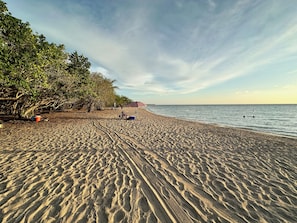 A beach with footprints, a few people, and a distant shoreline. - Modern 4 bedroom loft, open-air living, private pool and power generator (Cabo Rojo)