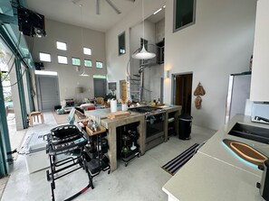 A spacious kitchen with a central island, a dining area with a sofa and chairs, and a view of the outdoors through large windows. - Modern 4 bedroom loft, open-air living, private pool and power generator (Cabo Rojo)