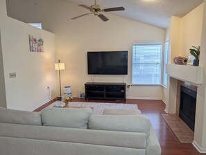Ein Wohnzimmer mit einer Couch, einem Flachbildfernseher, einem Kamin und einem Deckenventilator.