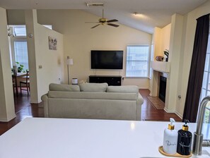Un salon comprenant un canapé, un téléviseur à écran plat, une cheminée et un coin repas avec une table et des chaises.