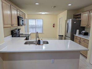 A kitchen with a large island, stainless steel appliances, wooden cabinets, and a window with blinds. - Relaxing & Peaceful San Antonio Home (San Antonio)