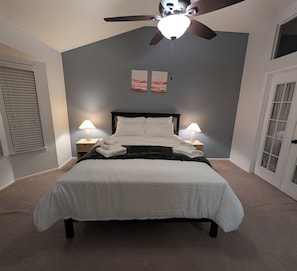 Ein Schlafzimmer mit einem Bett, zwei Nachttischlampen, einem Deckenventilator und zwei Wandbildern.