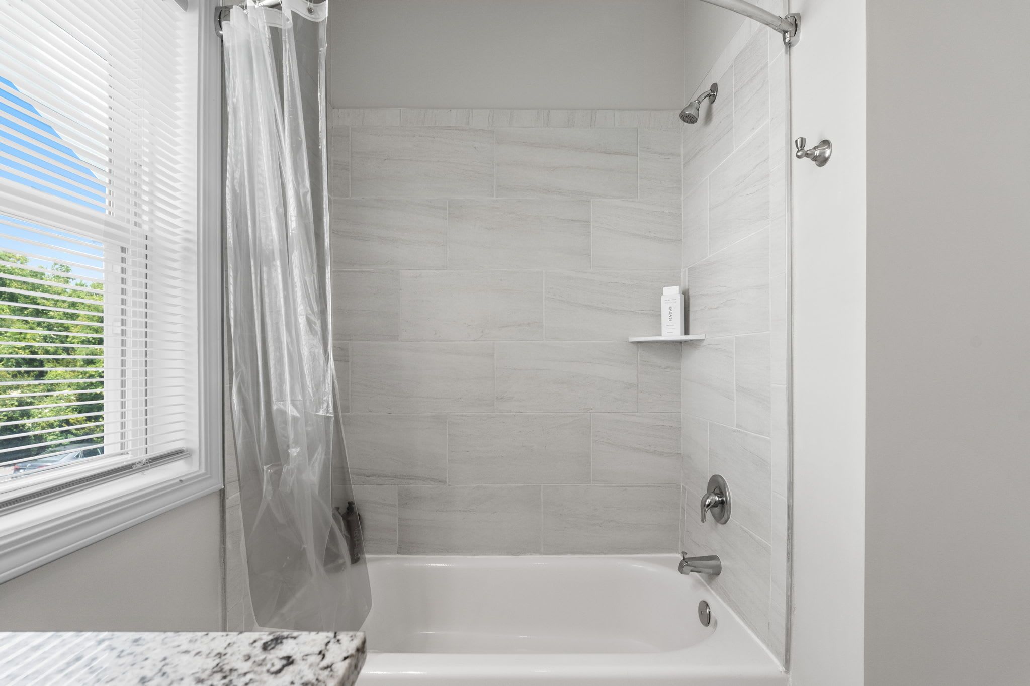 A bathroom with a shower, a bathtub, and a window with blinds.